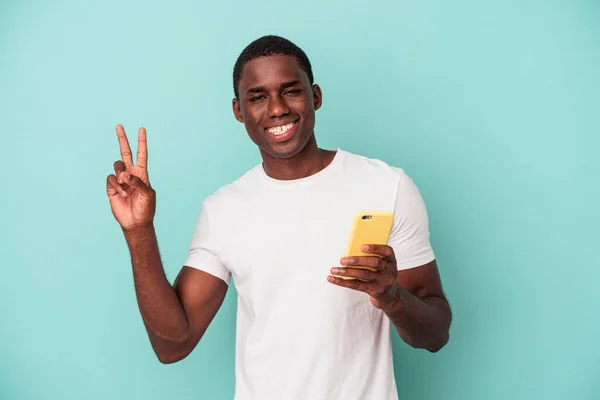 年轻的非裔美国人拿着一部蓝色背景的手机 兴高采烈 无忧无虑 手握和平的象征 — 图库照片