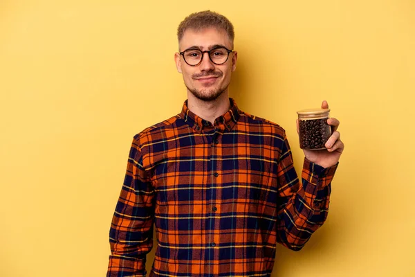 Młody Biały Mężczyzna Trzyma Słoik Kawy Odizolowany Żółtym Tle Szczęśliwy — Zdjęcie stockowe