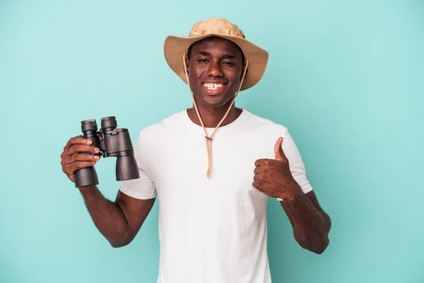 若いアフリカ系アメリカ人の男を保持双眼鏡青の背景笑顔と親指を上げる — ストック写真