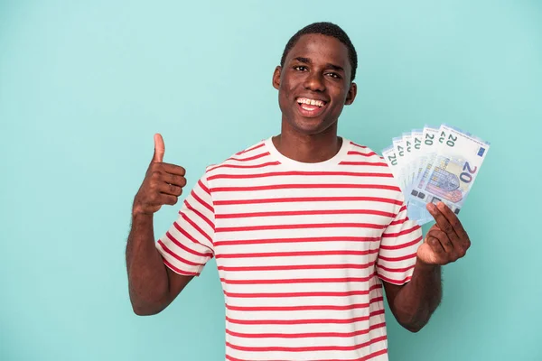 Joven Afroamericano Sosteniendo Billete Aislado Sobre Fondo Azul Sonriendo Levantando —  Fotos de Stock