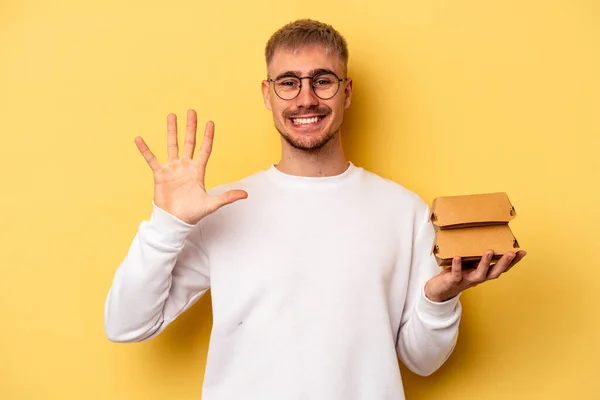 Young Caucasian Man Holding Burger Isolated Yellow Background Smiling Cheerful — Foto de Stock