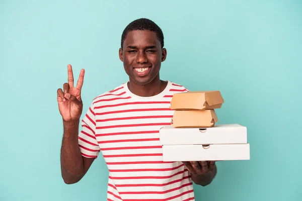Молодой Афроамериканец Держит Пиццу Бургеры Изолированные Синем Фоне Показывая Номер — стоковое фото