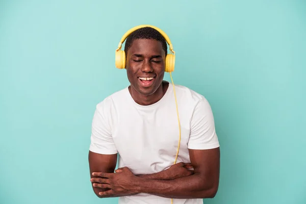 若いアフリカ系アメリカ人の男性が青い背景で孤立した音楽を聞いて笑って楽しい — ストック写真