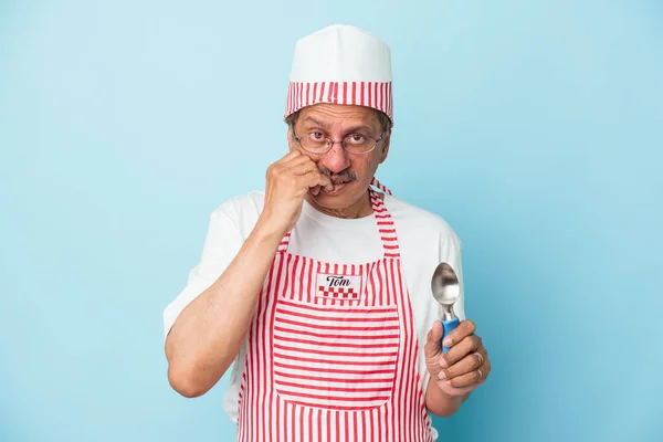 Senior indian ice cream man holding a scoop isolated on blue background biting fingernails, nervous and very anxious.