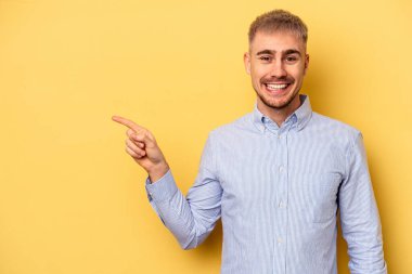 Sarı arka planda izole edilmiş genç beyaz adam işaret parmağıyla işaret ederek gülümsüyor..