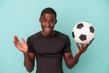 Futbol oynayan genç Afrikalı Amerikalı adam mavi arka planda izole edilmiş, şaşırmış ve şok olmuştu..