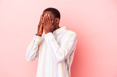 Genç Afro-Amerikalı adam pembe arka planda izole edilmiş. Gözleri elleriyle kapamaktan korkuyor..