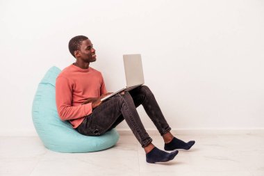 Beyaz arka planda izole edilmiş dizüstü bilgisayar kullanan genç Afrikalı Amerikalı adam gülümsüyor, neşeli ve keyifli görünüyor..