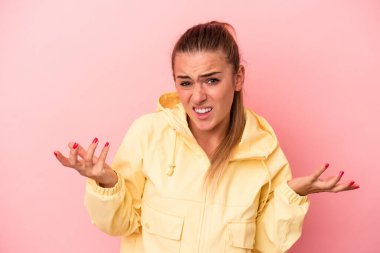 Pembe arka planda izole edilmiş genç bir Rus kadın şüpheye düşüp omuz silkiyor..