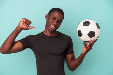 Mavi arka planda izole bir şekilde futbol oynayan genç Afrikalı Amerikalı adam gururlu ve kendinden emin hissediyor..