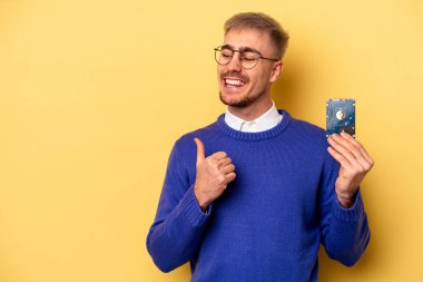 Young computer man isolated on yellow background points with thumb finger away, laughing and carefree.