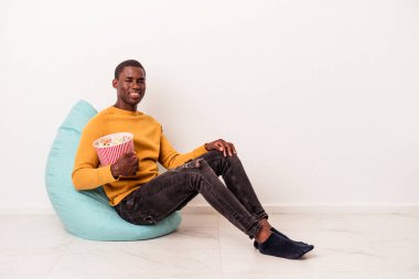 Beyaz arka planda izole edilmiş patlamış mısır yiyen genç Afrikalı Amerikalı adam mutlu, güler yüzlü ve neşeli..