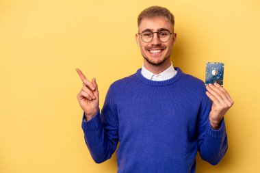 Young computer man isolated on yellow background smiling and pointing aside, showing something at blank space.