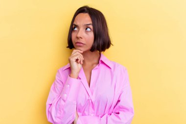 Sarı arka planda izole edilmiş genç melez kadın şüpheli ve şüpheci bir ifadeyle yana bakıyor..