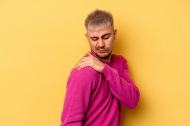 Sarı arka planda izole edilmiş, omuz ağrısı olan genç beyaz bir adam..