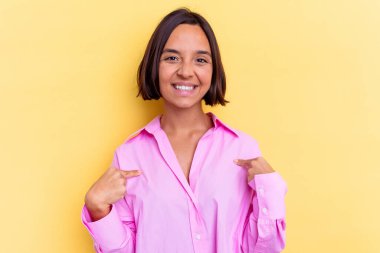 Sarı arka planda izole edilmiş genç bir ırk kadını gömlek fotokopisini elle gösteriyor, gururlu ve kendinden emin.