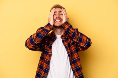 Sarı arka planda izole edilmiş genç beyaz adam ellerini başının üstünde tutarak neşe içinde gülüyor. Mutluluk kavramı.