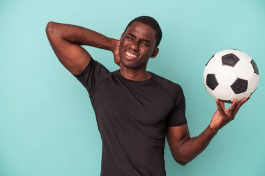 Futbol oynayan genç Afrikalı Amerikalı adam mavi arka planda izole edilmiş kafasının arkasına dokunuyor, düşünüyor ve bir seçim yapıyor..