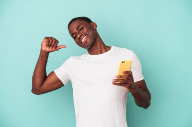 Mavi arka planda izole edilmiş cep telefonu tutan genç bir Afrikalı Amerikalı gururlu ve kendinden emin hissediyor, örnek olarak.