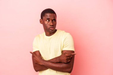 Genç Afrikalı Amerikalı adam pembe arka planda iki seçenek arasında seçim yapmaya çalışıyor..