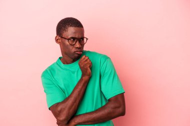 Genç Afrikalı Amerikalı bir adam pembe arka planda izole edilmiş, kafası karışmış, şüpheli ve güvensiz hissediyor..
