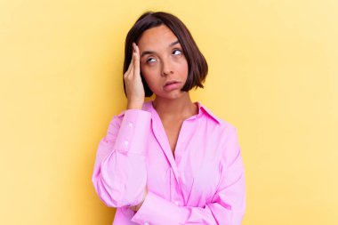 Sarı arka planda soyutlanmış genç melez bir kadın yorgun ve uykulu bir şekilde ellerini başının üstünde tutuyor..