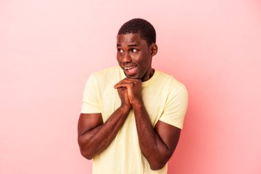 Genç Afrikalı Amerikalı bir adam pembe arka planda izole edilmiş şans için dua ediyor, hayrete düşüyor ve ağzını açıyor..