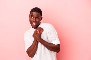 Pembe arka planda izole edilmiş genç Afrikalı Amerikalı ellerini çenesinin altında tutuyor ve mutlu bir şekilde yan tarafa bakıyor..