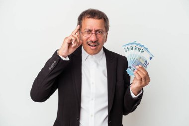 Middle aged indian business man holding bills isolated on white background showing a disappointment gesture with forefinger.