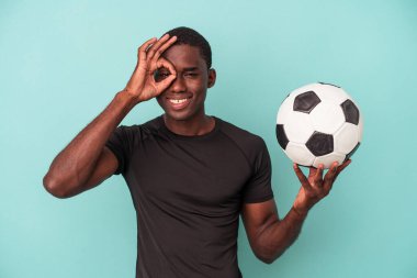 Genç Afro-Amerikalı adam mavi arka planda izole bir şekilde futbol oynuyor..