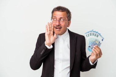 Middle aged indian business man holding bills isolated on white background is saying a secret hot braking news and looking aside