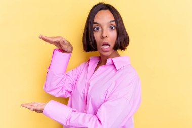 Sarı arka planda izole edilmiş genç bir ırk kadını elleri arasında bir kopya alanı tutarken şok ve şaşkınlık yaşadı..