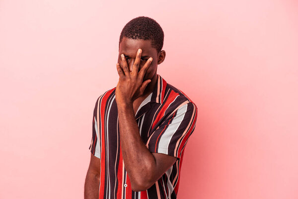 Young African American man isolated on pink background blink at the camera through fingers, embarrassed covering face.