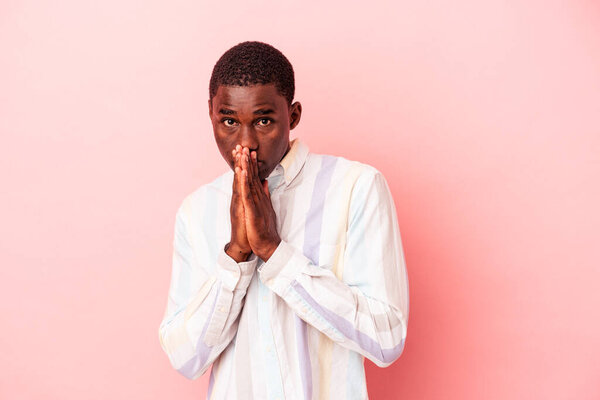 Young African American man isolated on pink background praying, showing devotion, religious person looking for divine inspiration.