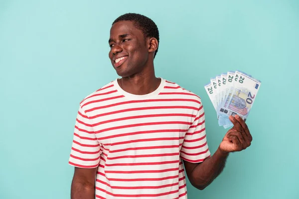 Mladý Afroameričan Drží Bankovky Izolované Modrém Pozadí Dívá Stranou Úsměvem — Stock fotografie