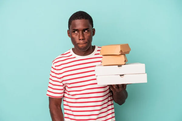 Mladý Afroameričan Drží Pizzy Hamburgery Izolované Modrém Pozadí Zmatený Cítí — Stock fotografie