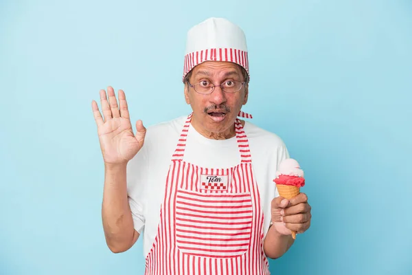 Senior american ice cream man holding an ice cream isolated on blue background surprised and shocked.