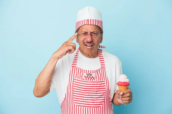 Senior american ice cream man holding an ice cream isolated on blue background showing a disappointment gesture with forefinger.