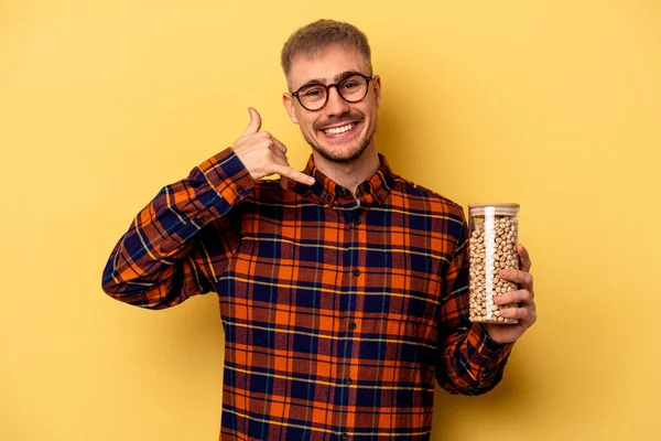 Young Caucasian Man Holding Chickpeas Isolated Yellow Background Showing Mobile — Stock fotografie