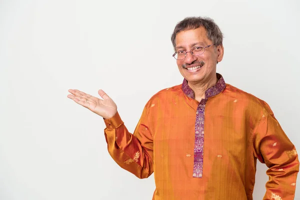 Senior indian man wearing a Indian costume isolated on white background showing a copy space on a palm and holding another hand on waist.