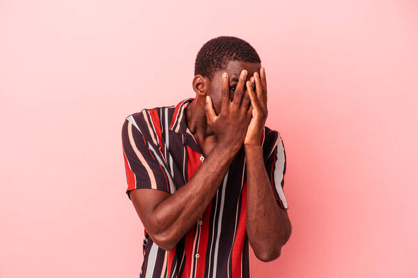 Young African American man isolated on pink background blink through fingers frightened and nervous.