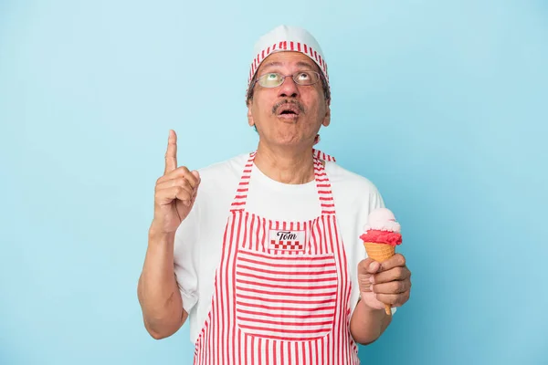 Senior american ice cream man holding an ice cream isolated on blue background pointing upside with opened mouth.