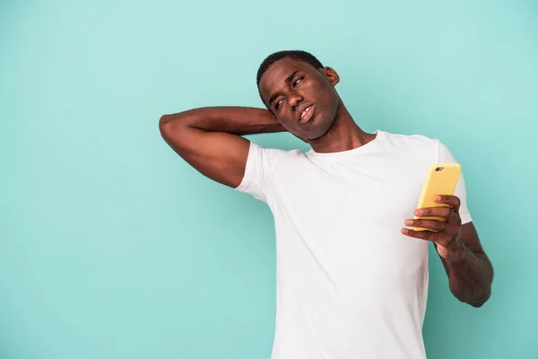 年轻的非裔美国人拿着一部蓝色背景的手机 背对着头 思考着 做出了选择 — 图库照片