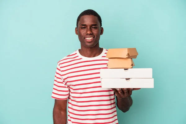 Молодой Афроамериканец Держит Пиццу Бургеры Голубом Фоне Счастливый Улыбающийся Веселый — стоковое фото