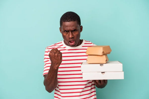 Mladý Afroameričan Drží Pizzy Burgery Izolované Modrém Pozadí Ukazující Pěst — Stock fotografie