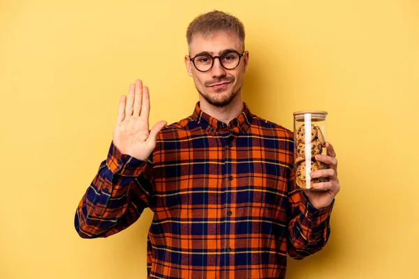 Young Caucasian Man Holding Cookies Jar Isolated Yellow Background Standing — Zdjęcie stockowe