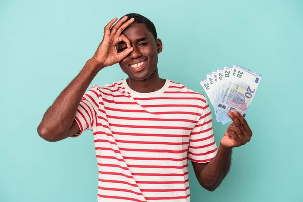 若いですアフリカ系アメリカ人男性保持A銀行券隔離上の青の背景励起保つ上でOkジェスチャー上の目 — ストック写真