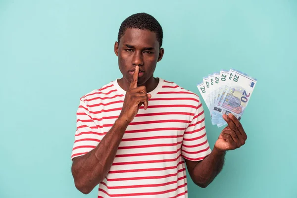 Joven Afroamericano Sosteniendo Billetes Aislados Sobre Fondo Azul Guardando Secreto —  Fotos de Stock