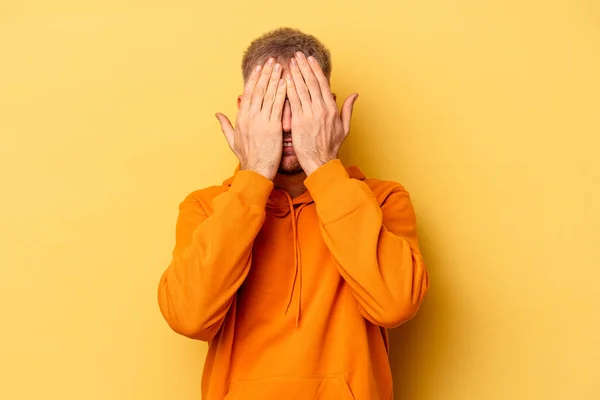 Young caucasian man isolated on yellow background having fun covering half of face with palm.