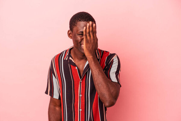 Young African American man isolated on pink background having fun covering half of face with palm.